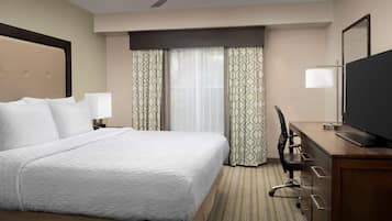 Una habitación de hotel con una cama grande, un escritorio con ordenador, una silla y un televisor.