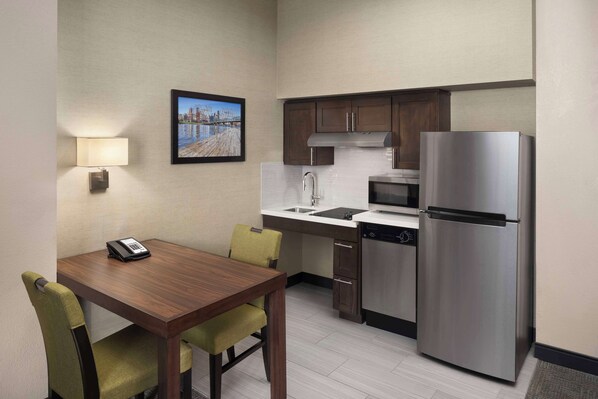 A compact kitchen with a refrigerator, microwave, sink, and a dining table with chairs.