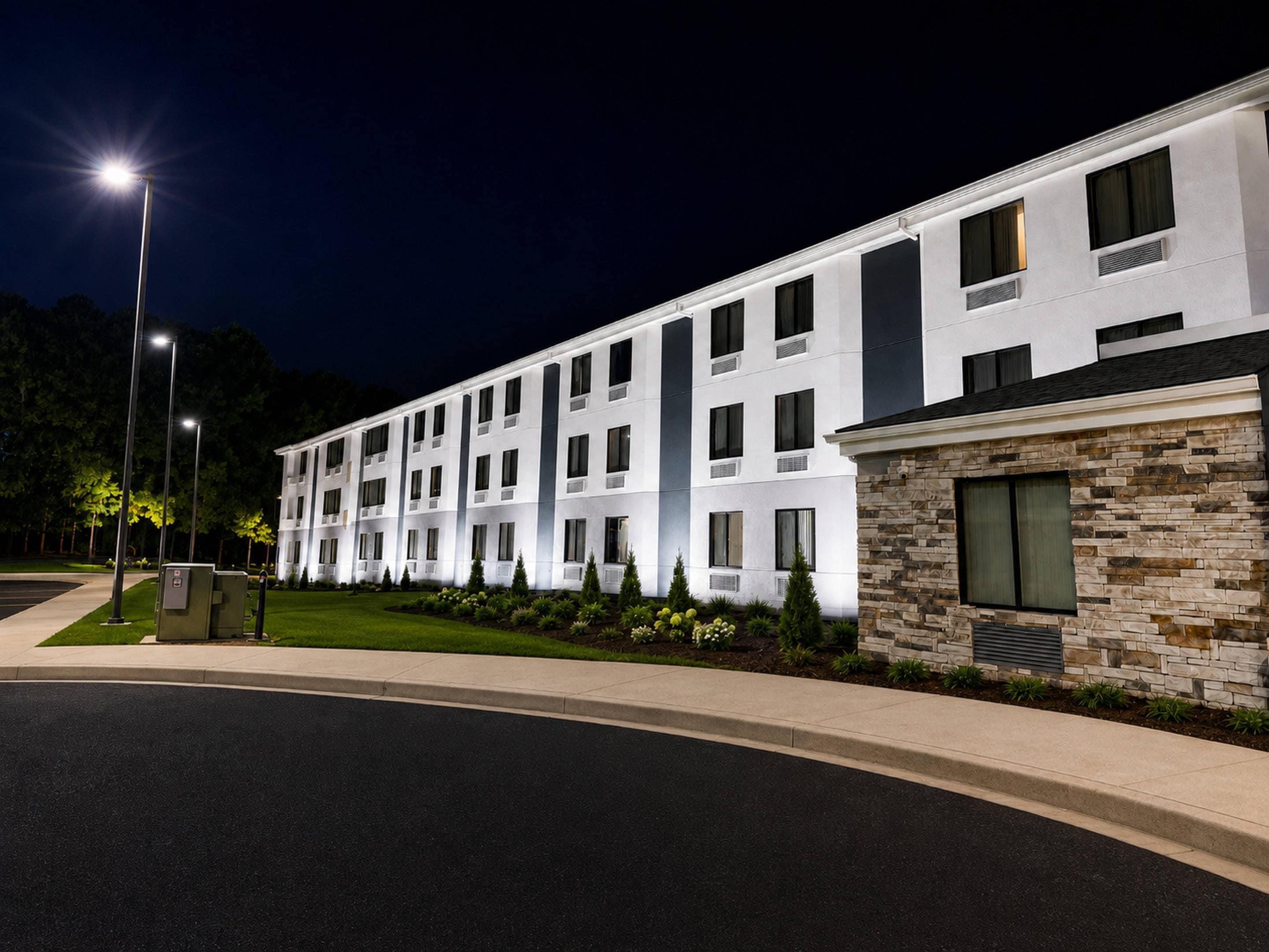 Un hotel de varios pisos con diseño moderno, que presenta un muro de acento de piedra y una fachada bien iluminada.