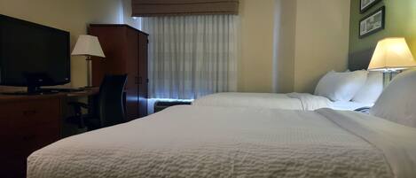 A hotel room with a bed, a desk with a TV, a chair, a wardrobe, and a window with curtains.