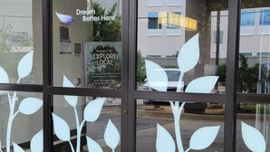 Une entrée d’immeuble avec des portes en verre ornées de motifs de feuilles et une enseigne sur laquelle on peut lire : « Ici, vos rêves prennent vie. »