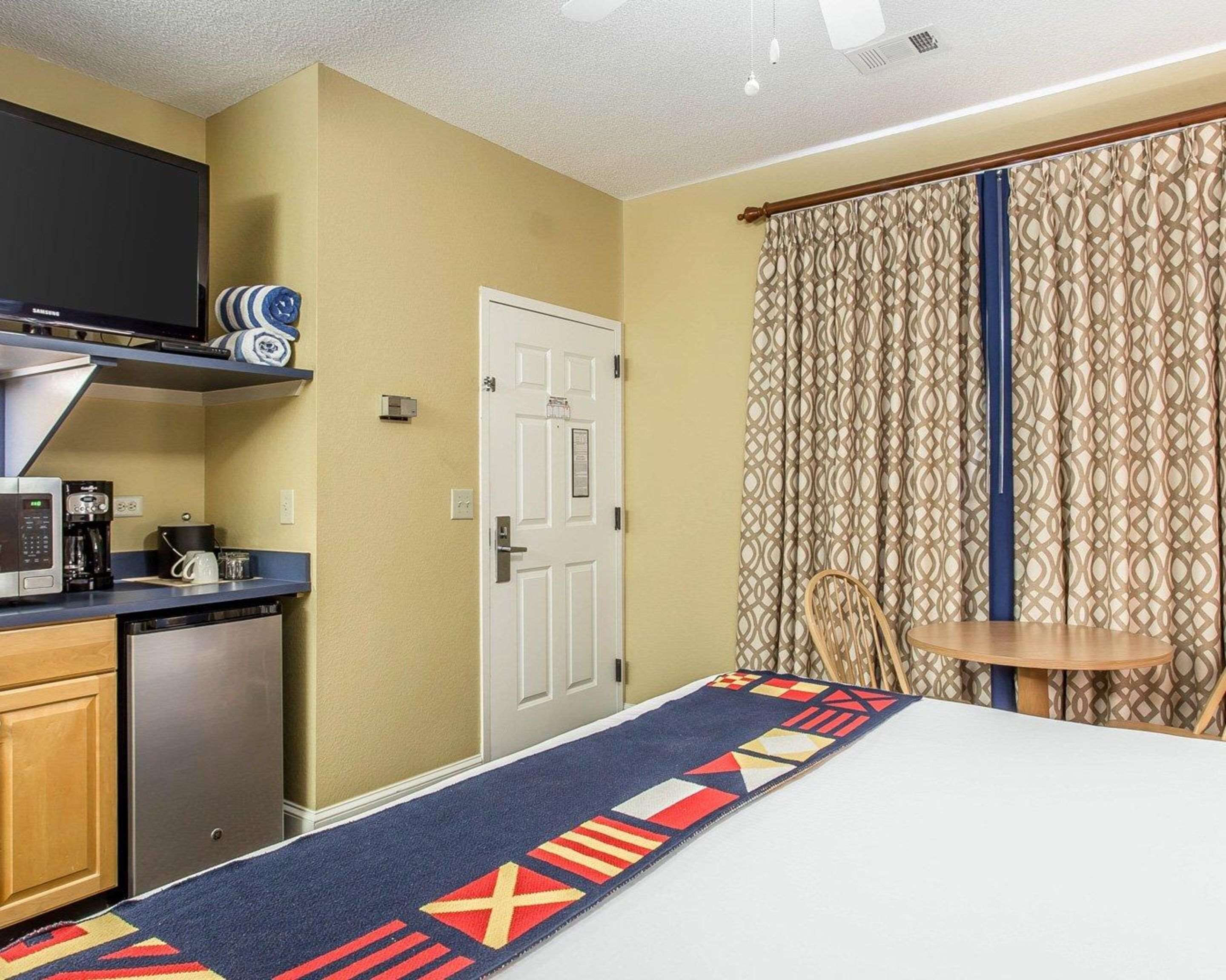A compact hotel room with a kitchenette, a bed, a small table, and a curtain with a geometric pattern.