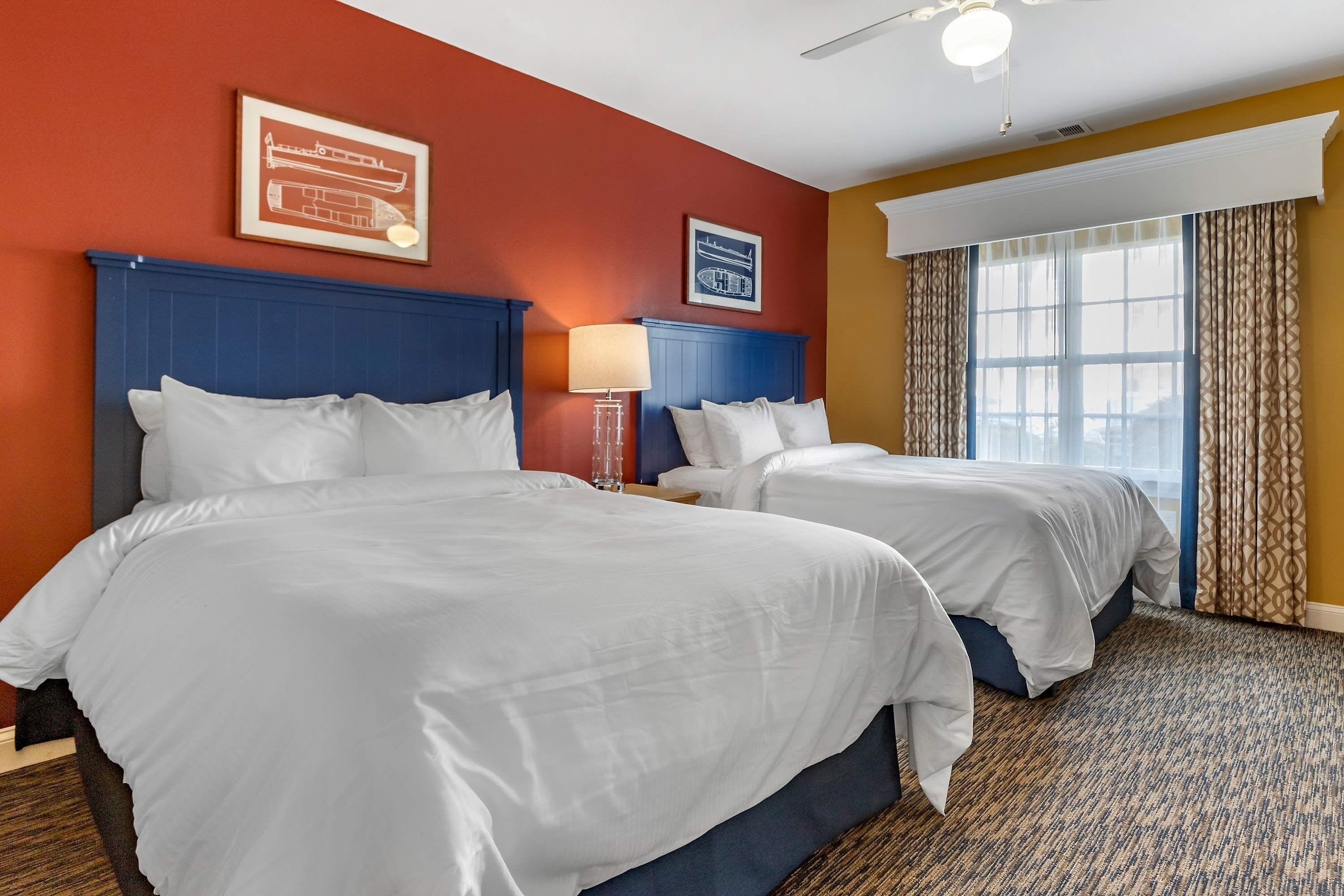 Une chambre d’hôtel avec deux lits, un ventilateur de plafond et une grande fenêtre avec des rideaux.