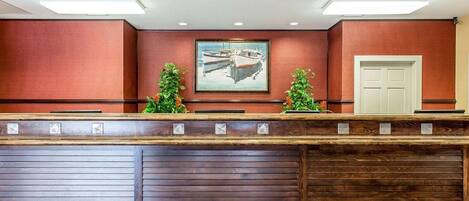 A reception desk with a wooden finish, a framed picture of boats on the wall, and a door to the right.