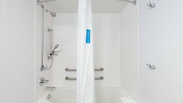 Une salle de bain moderne avec une douche à l’italienne, des barres d’appui et une baignoire blanche.