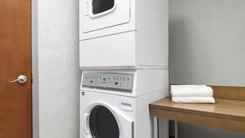 A stacked washer and dryer unit with a wooden bench and a towel on top.