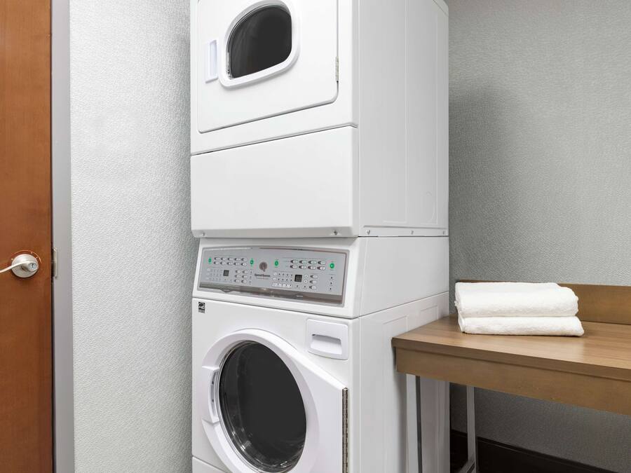 A stacked washer and dryer unit with a wooden bench and a towel on top.