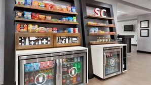 A snack display with various packaged foods and a refrigerated beverage dispenser. - Hampton Inn Simpsonville (Simpsonville)