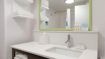 A modern bathroom with a white sink, a mirror with a green frame, and neatly folded towels on shelves.