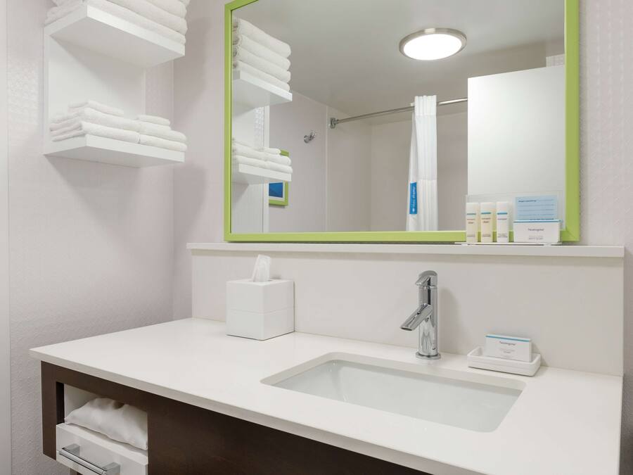 A modern bathroom with a white sink, a mirror with a green frame, and neatly folded towels on shelves.