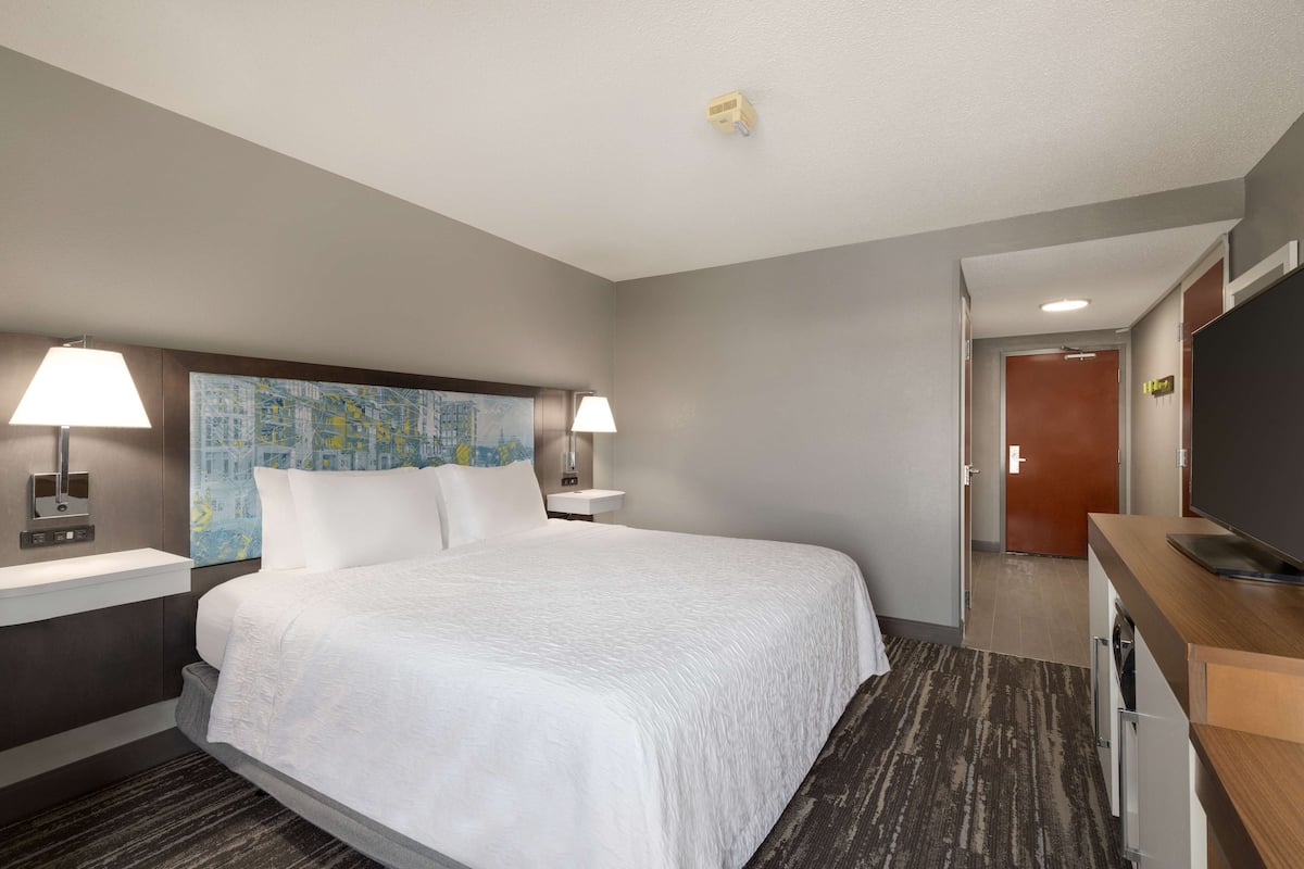 A hotel room with a large bed, two bedside lamps, a map on the headboard, a flat-screen TV, a wooden desk, and a washing machine.
