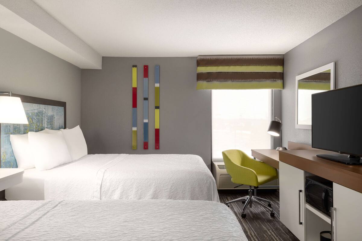 A hotel room with two beds, a desk with a chair, a television, and a window with curtains.