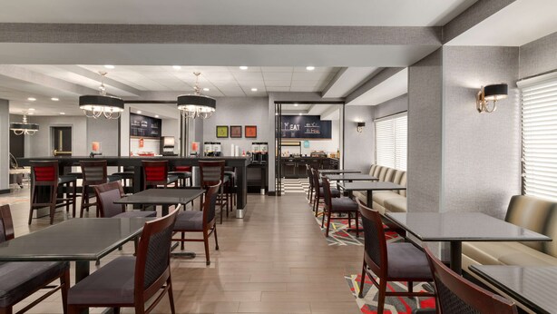 A modern restaurant with high tables and booths, a bar area, and a visible kitchen in the background. - Hampton Inn Simpsonville (Simpsonville)