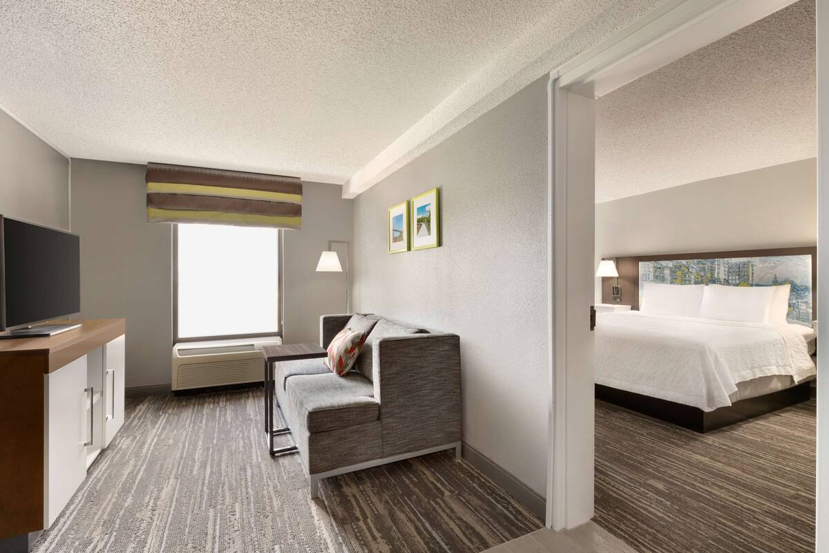 A hotel room with a sofa, a bed, a TV, and a window.