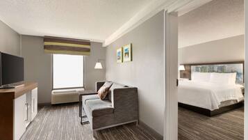 A hotel room with a sofa, a bed, a TV, and a window.