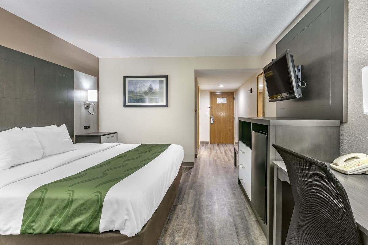 A hotel room with a bed, a desk, a chair, a TV, and a phone.