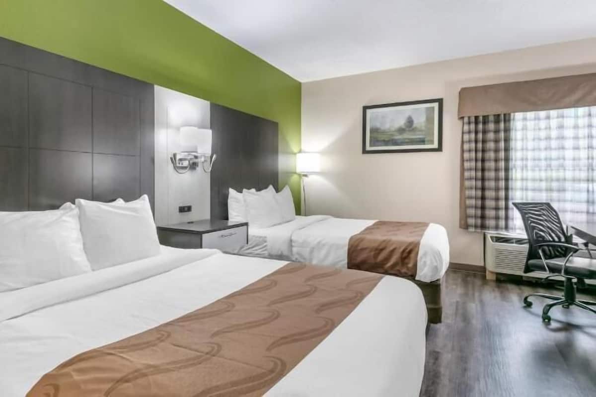 A hotel room with two beds, a desk, a chair, and a painting on the wall.