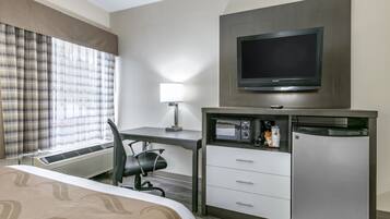 A hotel room with a bed, desk, chair, television, microwave, refrigerator, and a window with curtains.