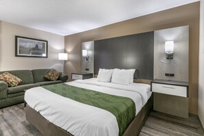A hotel room with a large bed, a green sofa, a nightstand with a lamp, and a wall-mounted light fixture. - Quality Inn Rogersville (Rogersville)