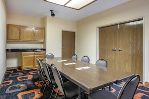 A conference room with a long table, chairs, a kitchenette, and a door.