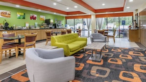 A modern hotel lobby with a green wall, a coffee station, seating areas, and large windows offering a view of the parking lot. - Quality Inn Rogersville (Rogersville)