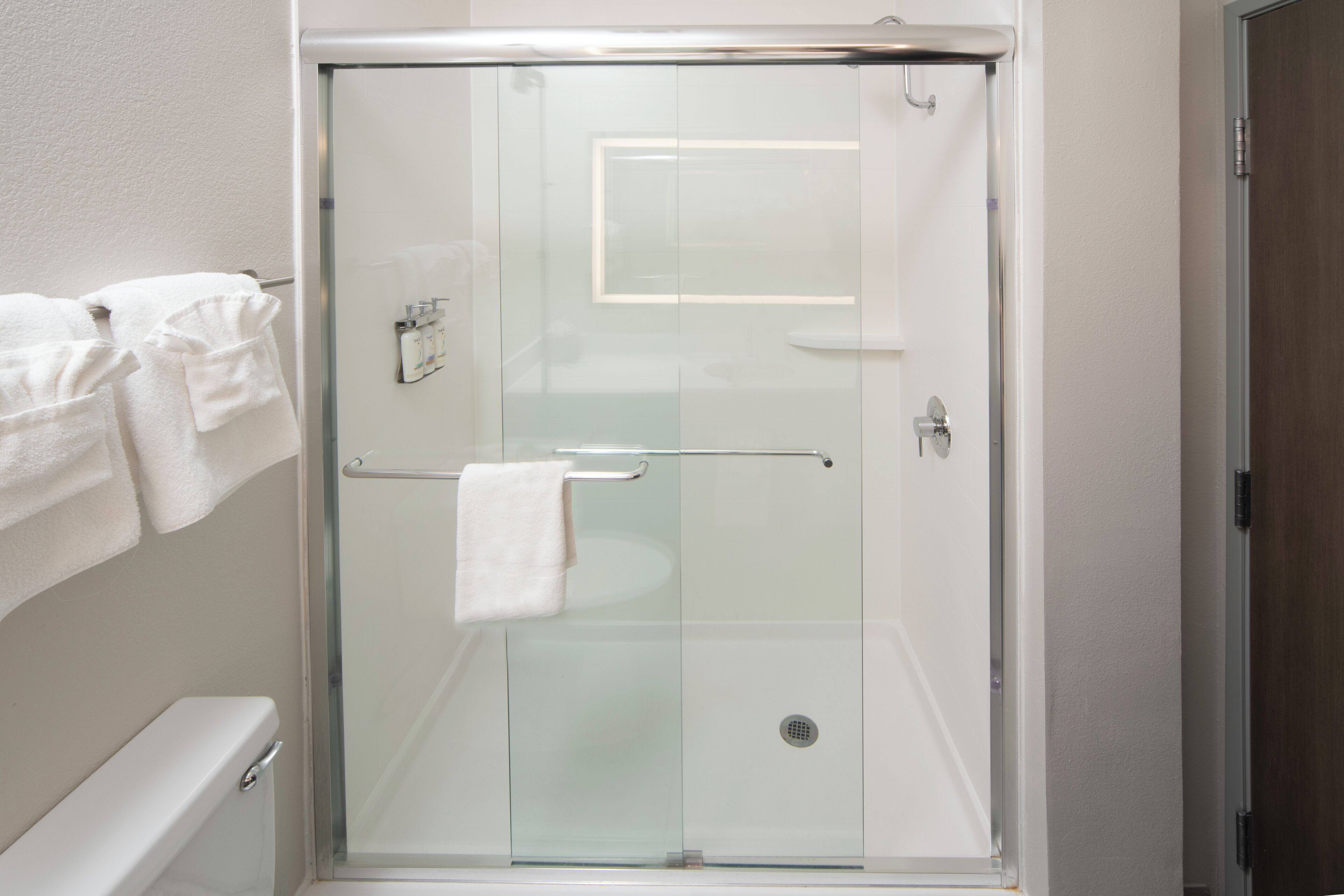 Cabina de ducha con paredes de vidrio y una toalla blanca colgada del picaporte.