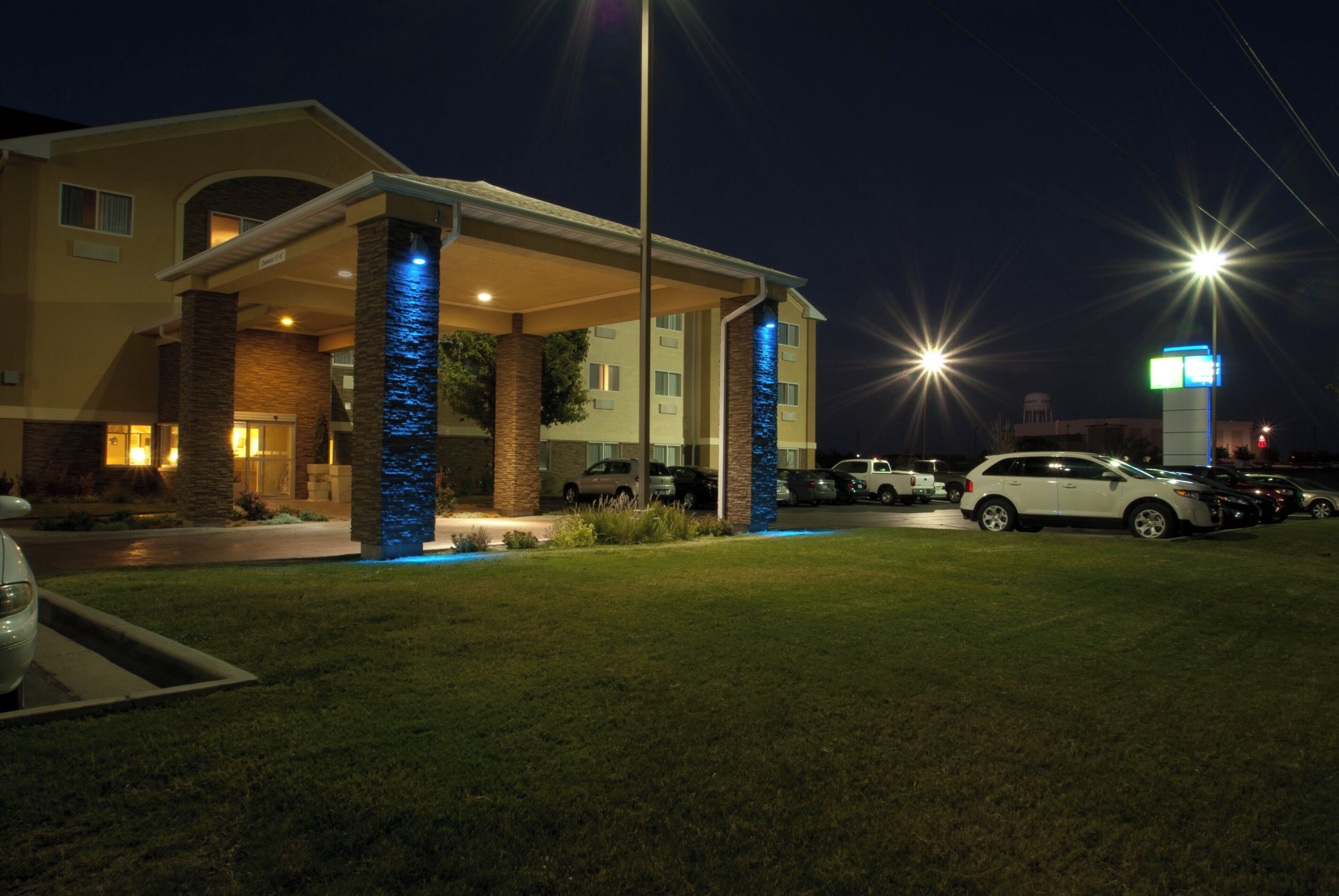 Un hotel con entrada cubierta, estacionamiento exterior y fachada bien iluminada por la noche.