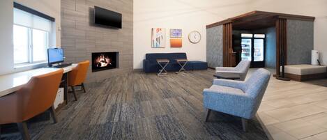 A modern lounge area with a flat-screen TV, a fireplace, comfortable seating, and a large window.