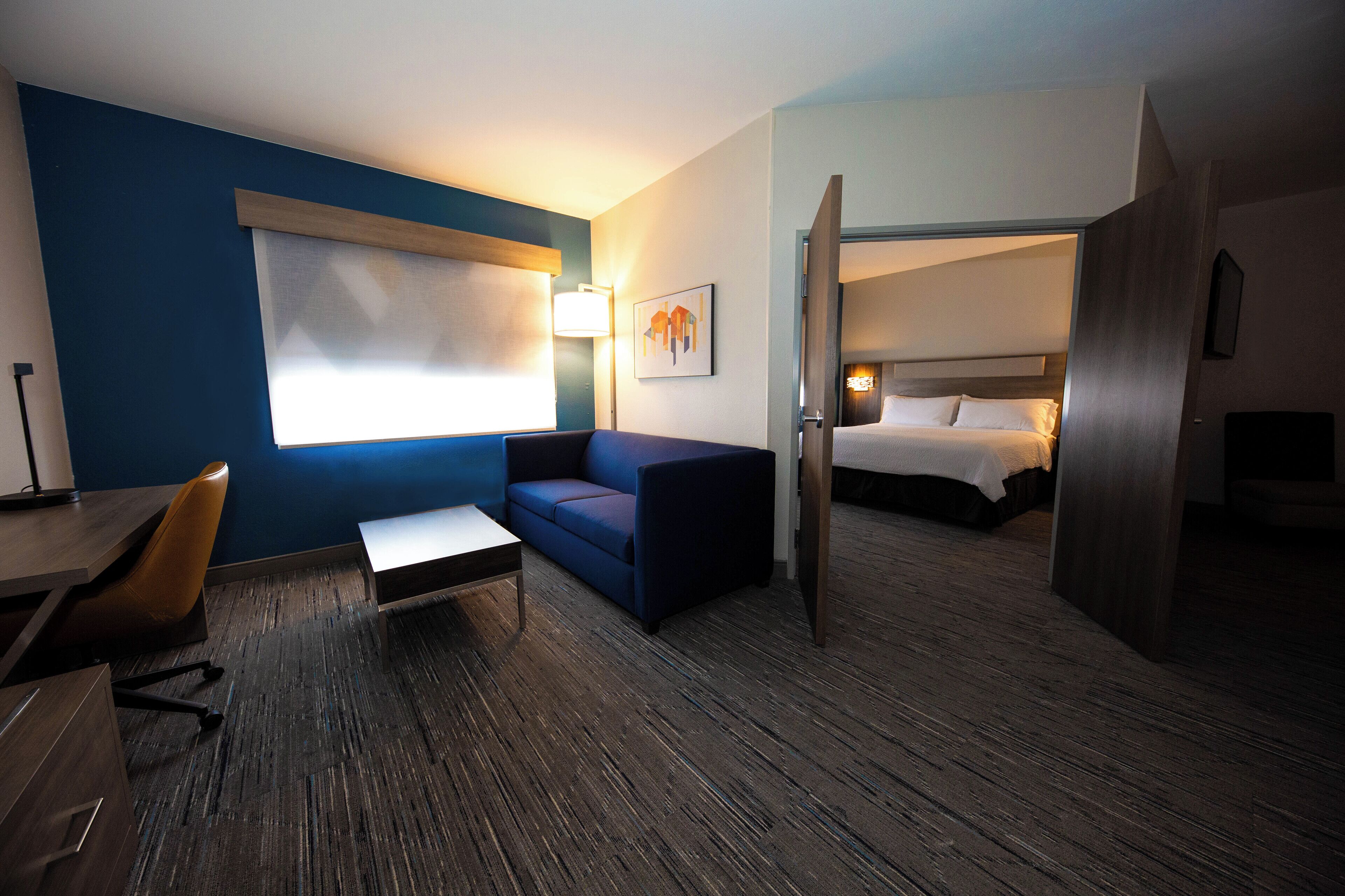 A hotel room with a blue wall, a bed, a desk, a chair, and a sofa.
