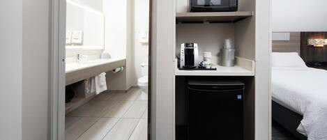 A hotel room with a bed, a small kitchenette with a microwave, a coffee machine, and a trash bin.