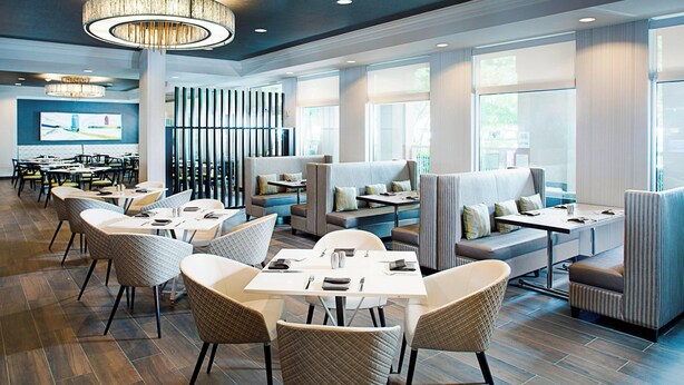 A modern restaurant with high tables and booths, large windows, and a chandelier. - Dallas Marriott Suites Medical/Market Center (Dallas)