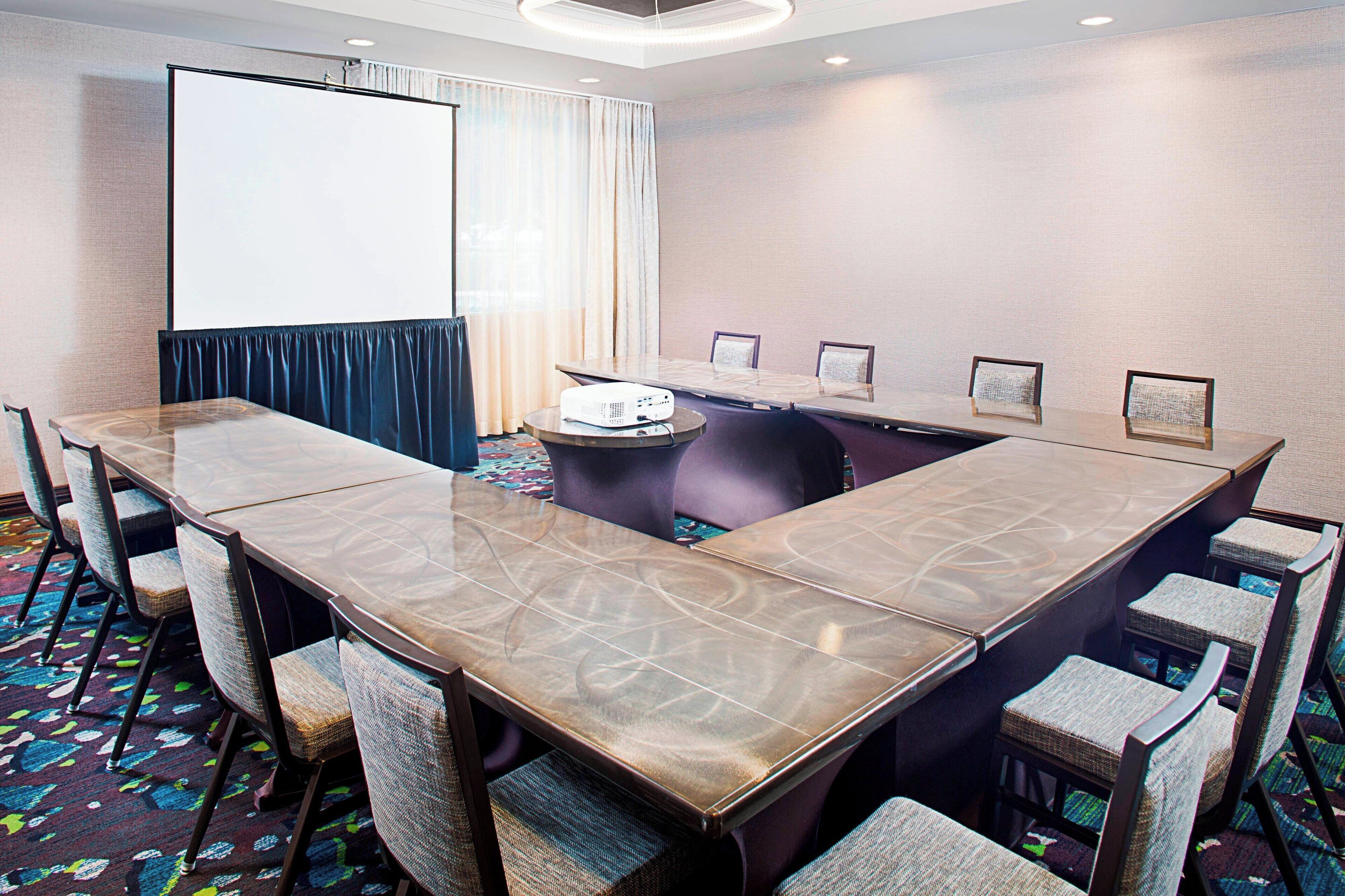 Un salón de conferencias con una mesa grande, sillas, un proyector y una pantalla.