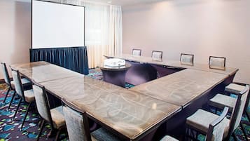 Uma sala de conferências com uma grande mesa, cadeiras, um projetor e uma tela.