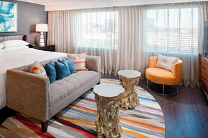 A hotel room with a bed, sofa, armchair, two round tables, and a large window with curtains. - Dallas Marriott Suites Medical/Market Center (Dallas)