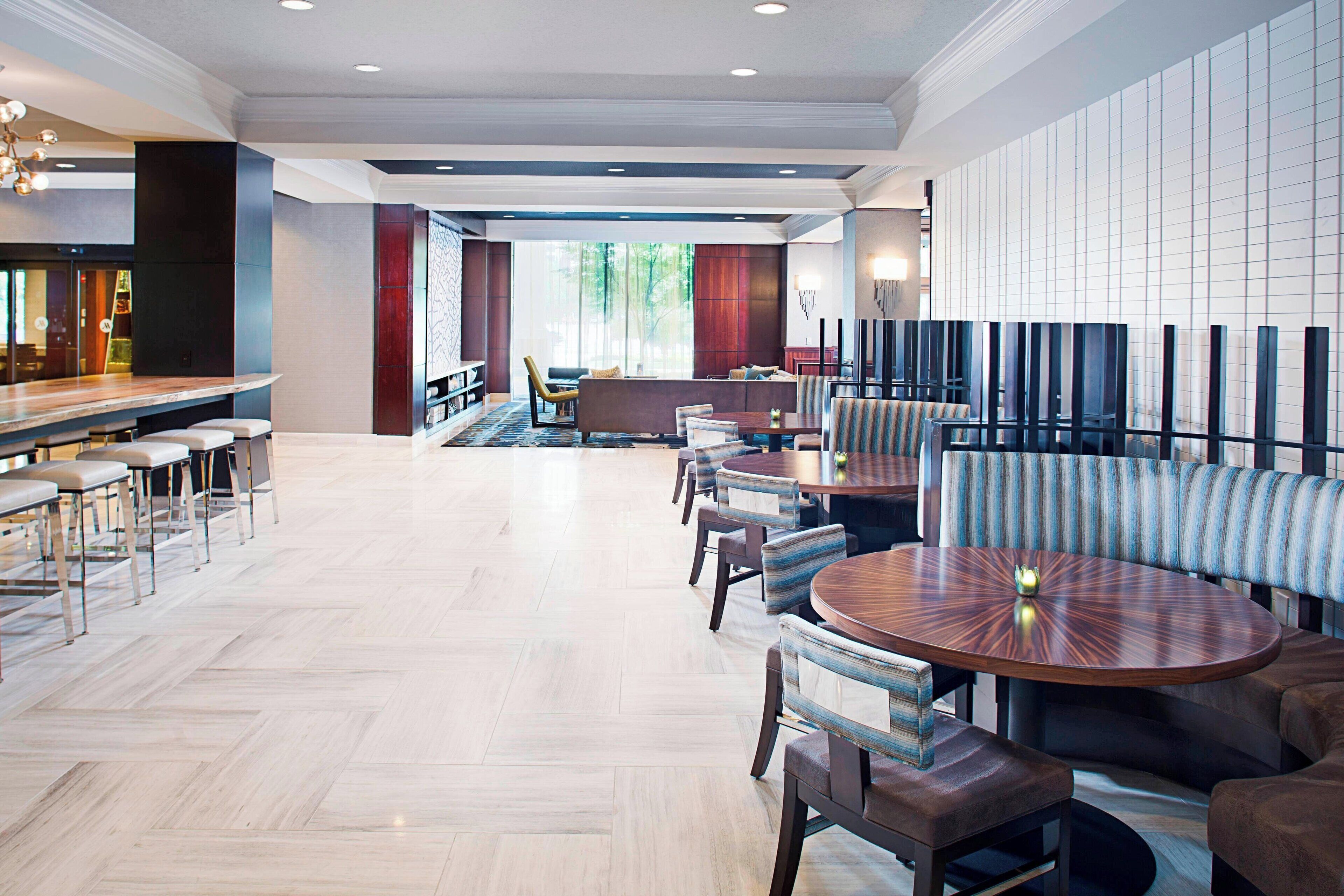 A modern hotel lobby with a bar area, seating arrangements, and a view of the outdoors.