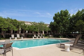 A swimming pool with lounge chairs and a table, surrounded by trees and a building in the background. - Dallas Marriott Suites Medical/Market Center (Dallas)
