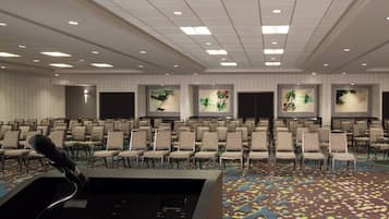 A conference room with rows of chairs, a podium with a microphone, and framed artwork on the walls.