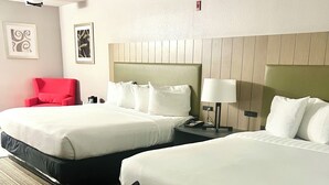 A hotel room with two beds, a red chair, a desk, and a lamp.