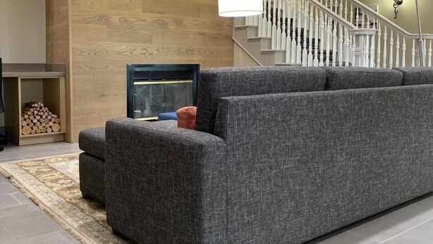 A modern living room with a gray sectional sofa, a fireplace, a staircase with white railings, and a wooden accent wall.