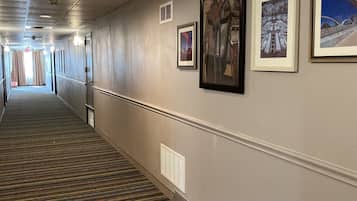 A hallway with a patterned carpet, framed pictures on the wall, and a tiled floor.