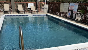 A swimming pool with a metal handrail, lounge chairs, and a fence with warning signs.