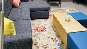 A living room with a sectional sofa, a small table, a chair, a clock, and a lamp.