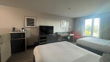 A hotel room with two beds, a desk with a computer, a television, and a red chair.