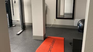 Zona de gimnasio con equipo de ejercicio, una colchoneta roja con el texto "campGladiator" y un espejo grande en la pared.