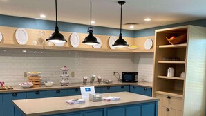 A modern kitchen with blue cabinets, a central island, pendant lighting, and a microwave.