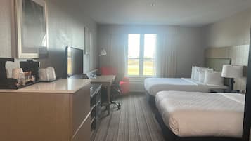 Habitación de hotel con dos camas, un escritorio con computadora, cafetera y ventana con cortinas.