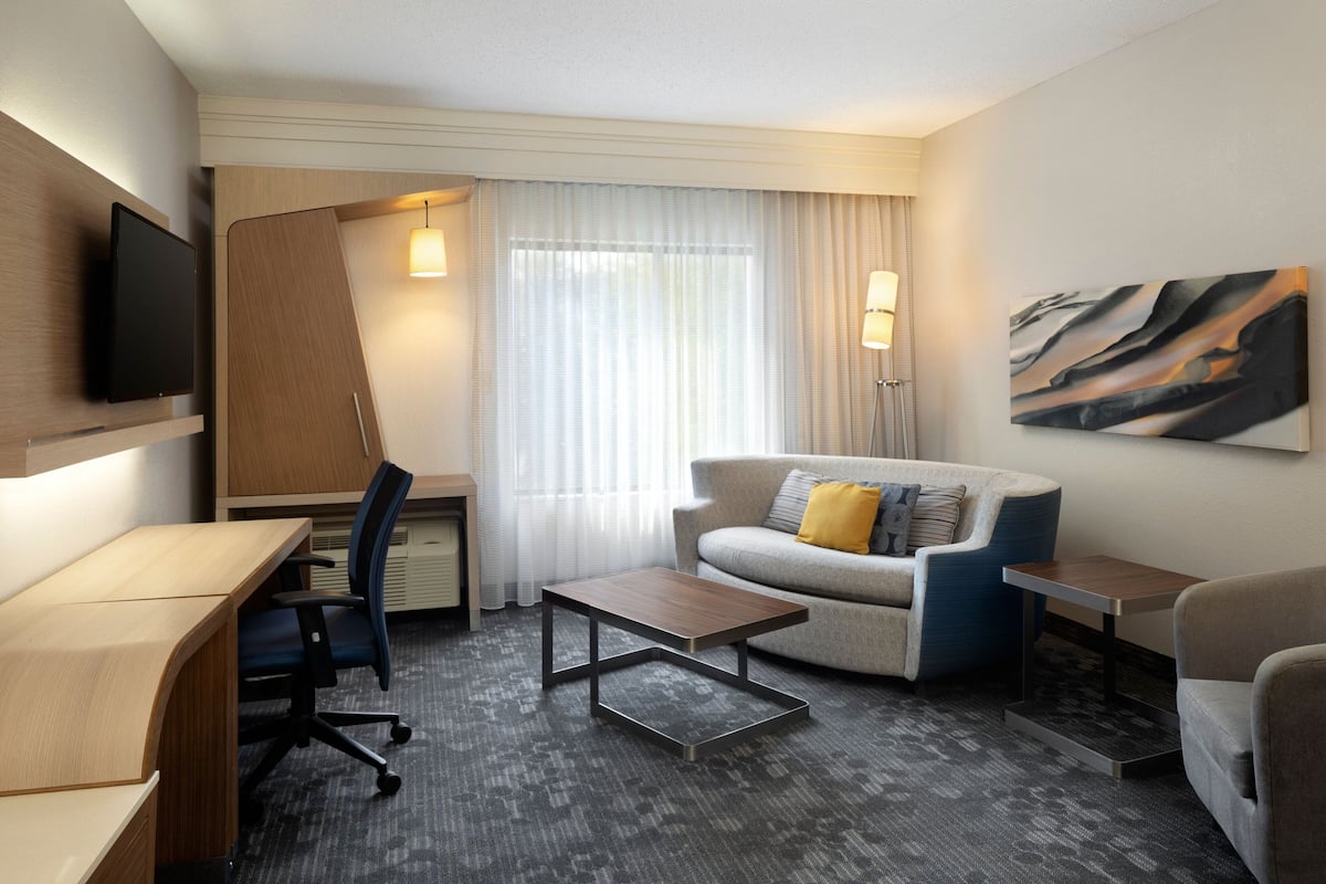 A hotel room with a desk, a sofa, a coffee table, and a TV mounted on the wall.