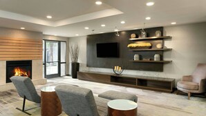 A modern living room with a fireplace, comfortable seating, a flat-screen TV, and built-in shelving. - Courtyard by Marriott Austin Round Rock (Round Rock)