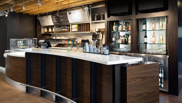 A modern bar area with a long counter, a coffee machine, and shelves with various bottles and glasses. - Courtyard by Marriott Austin Round Rock (Round Rock)
