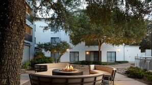 An outdoor seating area with a circular fire pit, cushioned seating, and a tree. - Courtyard by Marriott Austin Round Rock (Round Rock)